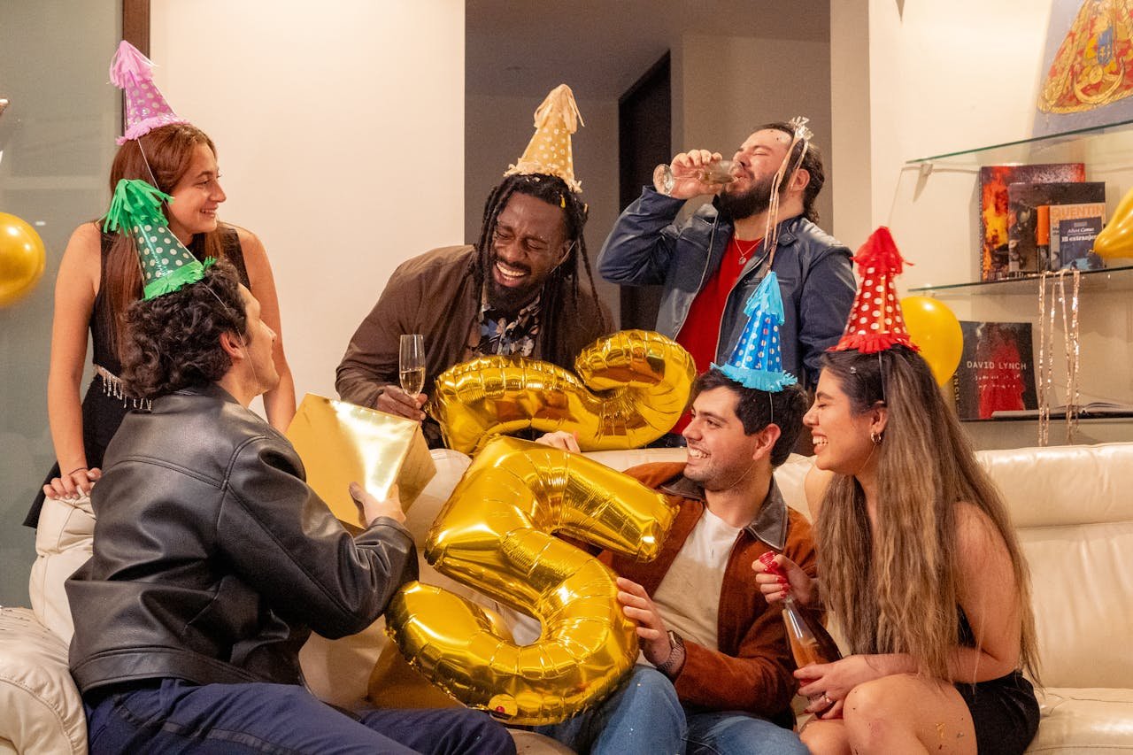 Happy group of friends celebrating a birthday with balloons and party hats.