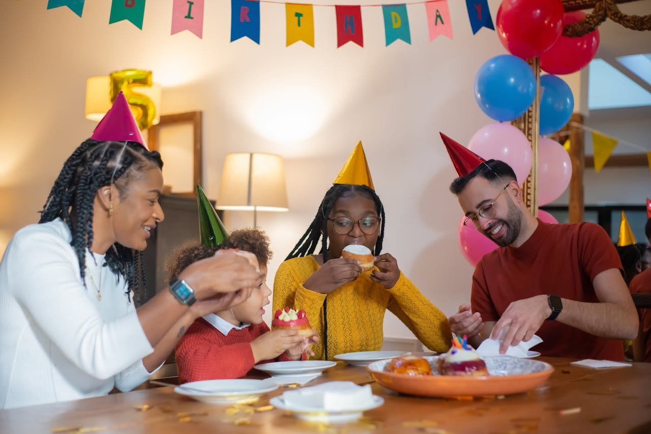 A cheerful family celebrating a birthday with cupcakes and party hats indoors.